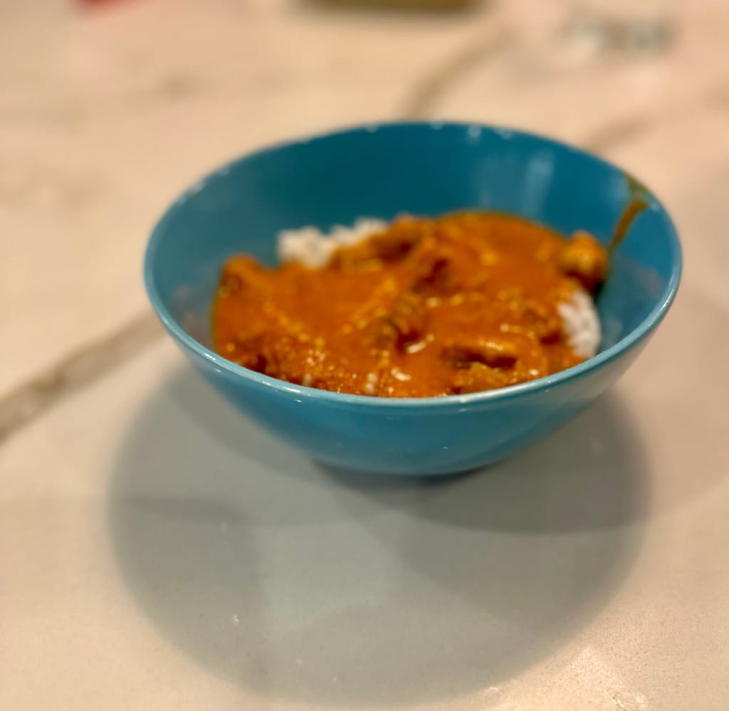 Photo of chicken tikka masala over rice in a blue bowl